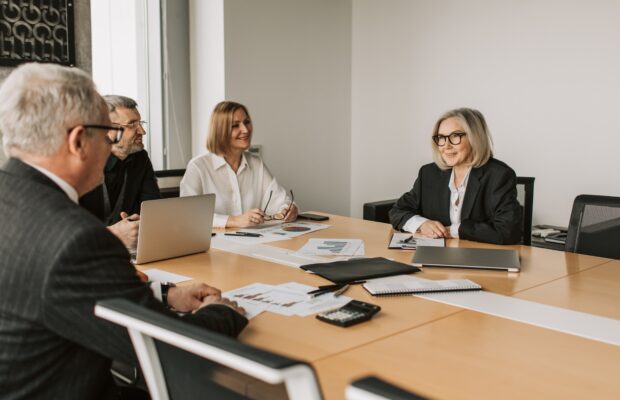 four payroll professionals dressed in business attire sitting around a small wooden desk in a conference room