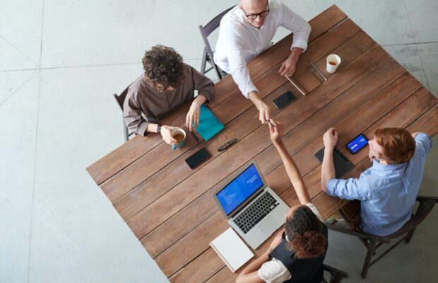 Four accountants having a payroll meeting around an oak wooden table with laptops and tablets visible