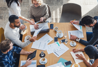 Six payroll professionals sitting around a wooden table having a meeting about outsourced payroll for uk clients