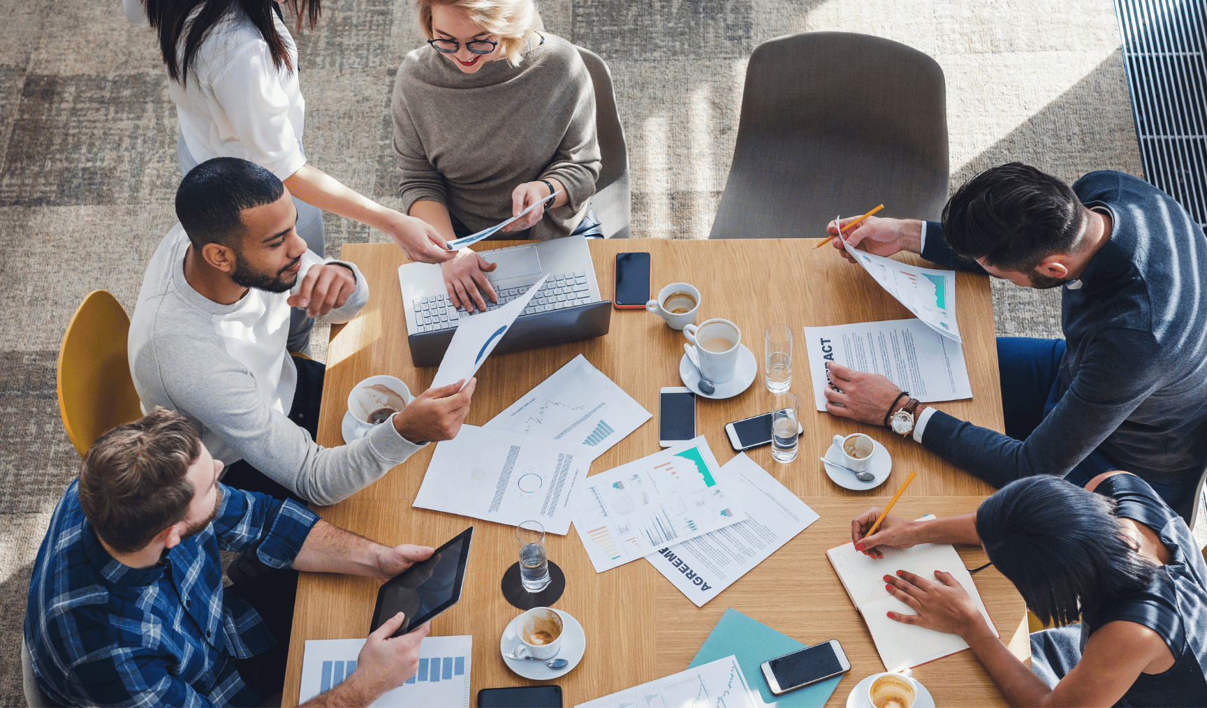 Six payroll professionals sitting around a wooden table having a meeting about outsourced payroll for uk clients